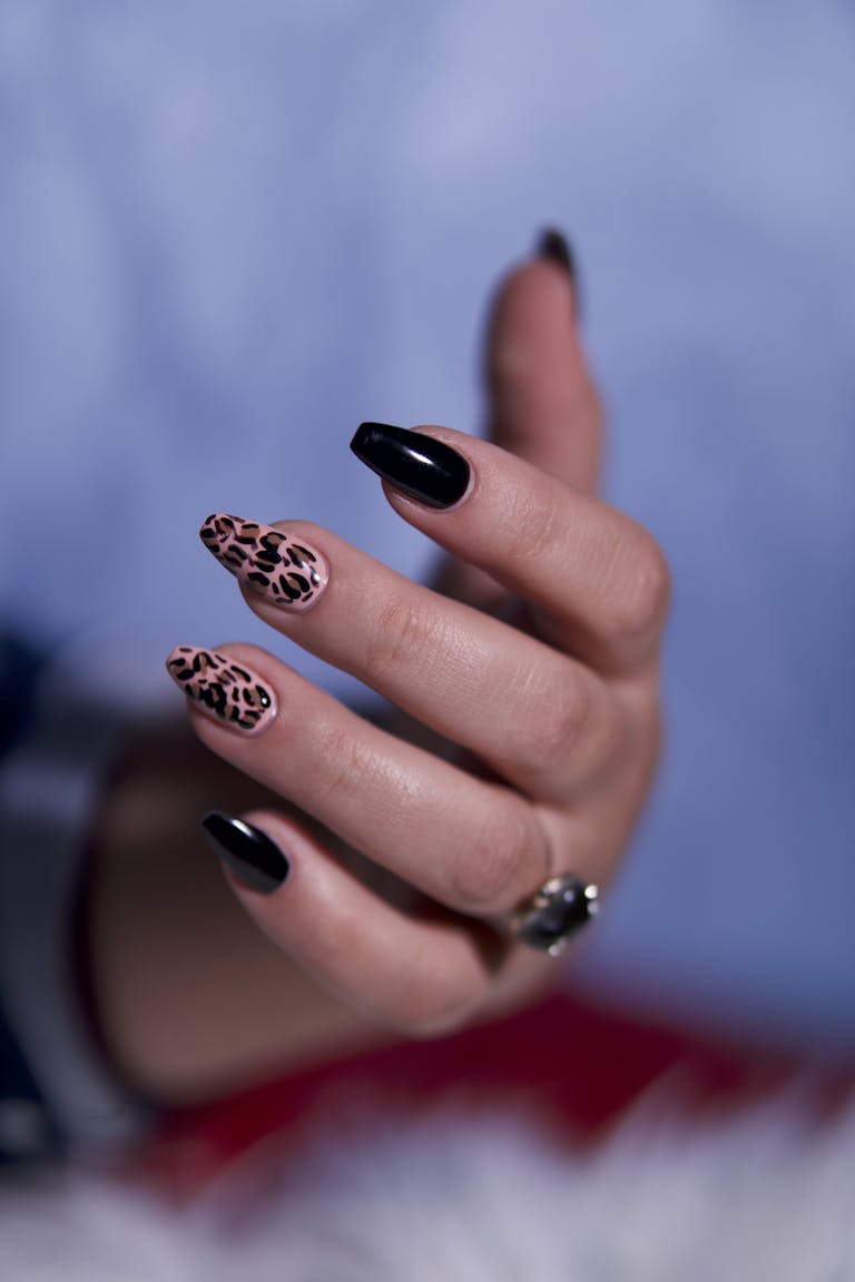 A close-up of a stylish hand featuring leopard print and black nail art, accessorized with a ring.
