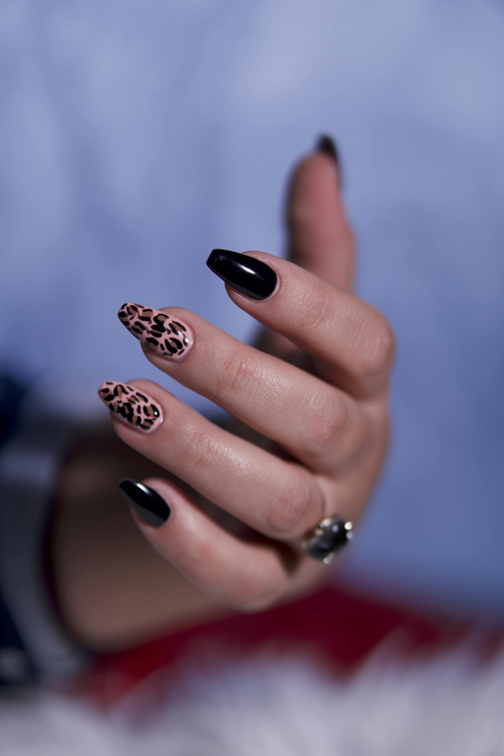 A close-up of a stylish hand featuring leopard print and black nail art, accessorized with a ring.