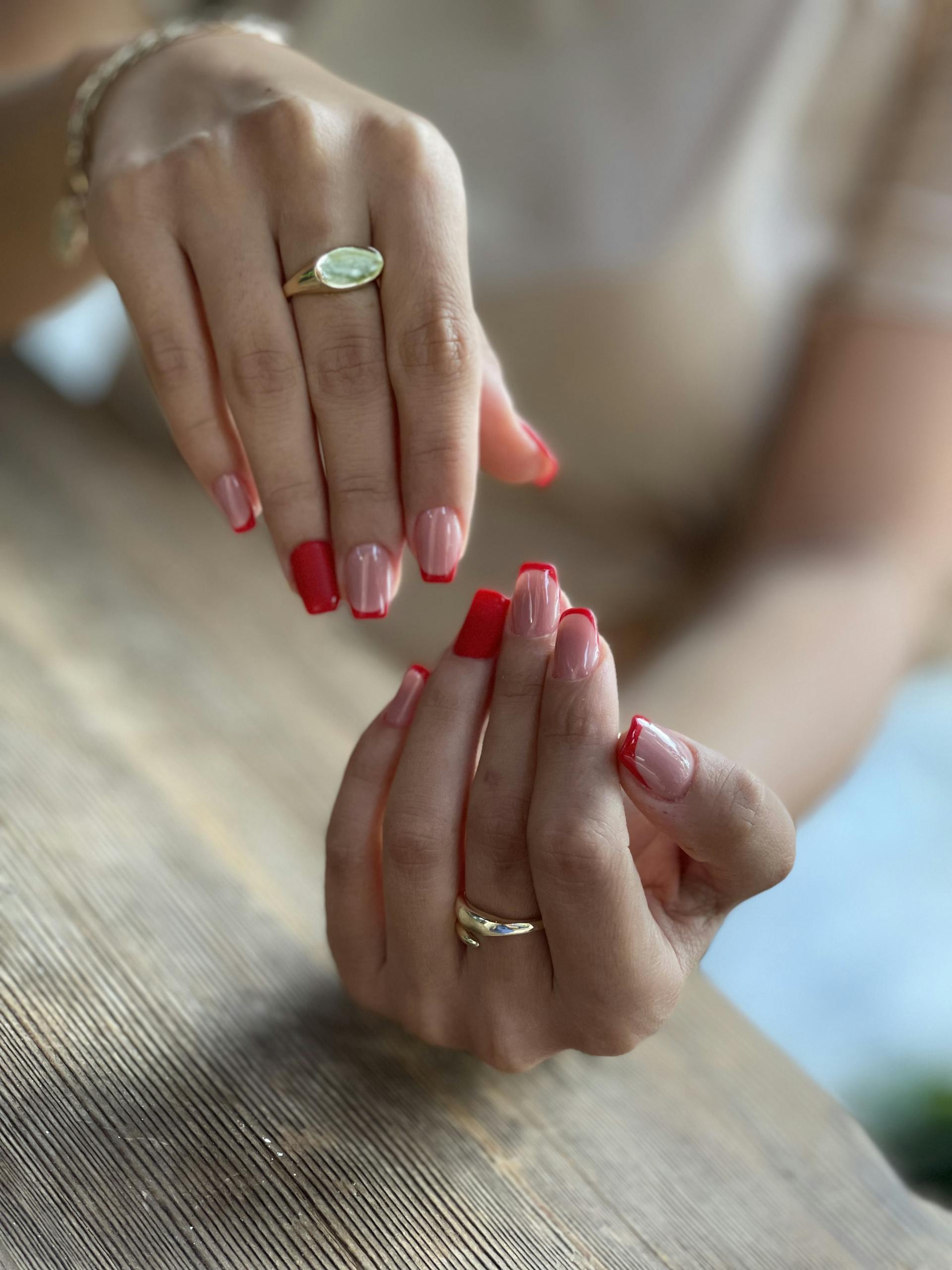 Close-up of elegant hands with red manicured nails and gold rings, showcasing style and beauty.