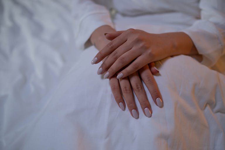 Close-up of hands resting, showcasing elegant nude nails on a white fabric.