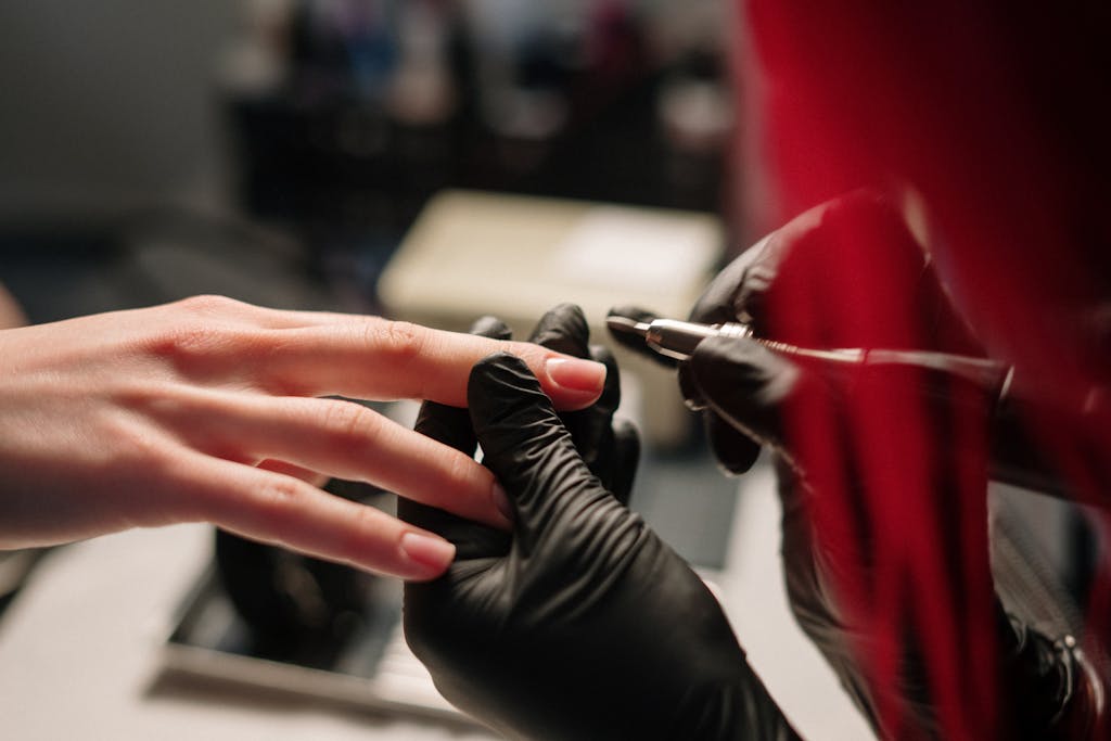 Detail of a manicure in progress with a technician wearing black gloves.