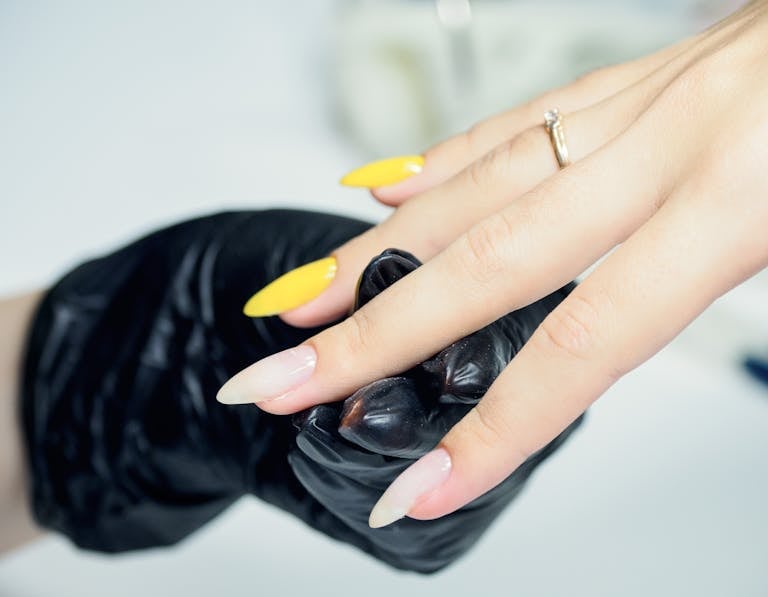 Detailed view of a hand with yellow manicured nails held by a gloved beautician.